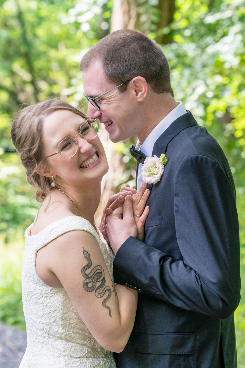 Brautpaar steht Körper an Körper. Sie stützt sich an seiner Brust und er hält ihre Hände. Dabei lächeln beide